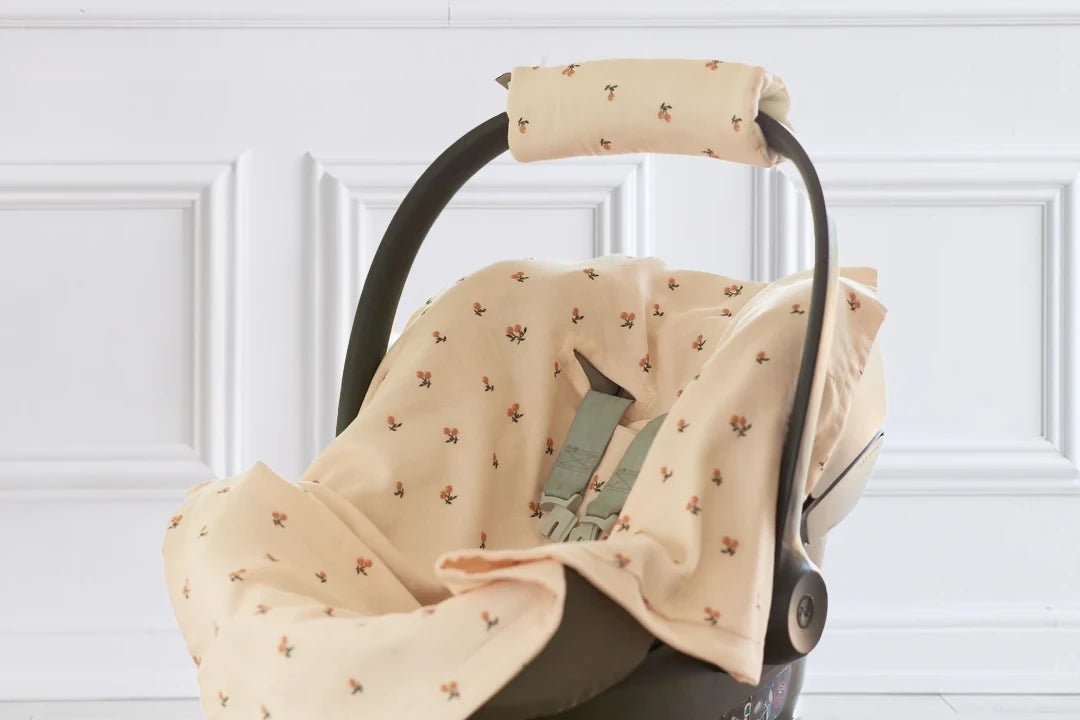 Eine Babyschale mit einem weichen, beigen Bezug mit kleinem Blumenmuster vor einer weißen, dekorativ getäfelten Wand.