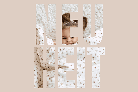 Ein lächelndes Baby, eingewickelt in eine gemusterte Decke, ist durch große ausgeschnittene Buchstaben zu sehen, die NEUHEIT auf einem beigen Hintergrund schreiben.