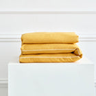 Ein Bettwäscheset Leinen gelb senfgelb von KraftKids liegt ordentlich gefaltet auf einem weißen rechteckigen Podest vor einer weißen Wand mit Zierleisten.