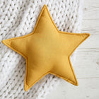 Das gelbe Sternkissen Leinen von KraftKids in Senfgelb liegt auf einer weißen klobigen Strickdecke auf hellem Holz - ein charmantes Detail fürs Kinderzimmer.
