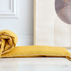 Ein KraftKids Bettumrandung Nestchen Leinen gelb senfgelb mit Krawatten und einem passenden Kissen liegt auf einem hellen Holzboden neben moderner abstrakter Kunst mit goldenen und braunen Kreislinien.