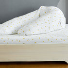 Ein weißes Holzbett mit gelb gemustertem Bettzeug steht in einem Zimmer mit grauen Wänden und Holzböden; ein KraftKids Stillkissenbezug Musselin gelbe Zitronen sorgt für Gemütlichkeit.