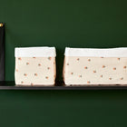 Zwei Stoffkörbchen aus Baumwolle von KraftKids, Modell "Körbchen Musselin Kirschen", mit weißem Rand stehen in unterschiedlichen Größen auf einem schwarzen Regal vor einer dunkelgrünen Wand.