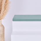 Eine hohe geflochtene Vase mit beigem Pampasgras steht neben weißen Stufen, auf denen die KraftKids GmbH Sitzauflage für Ikea TROFAST Doppelkrepp Grün Jade steht, vor einem schlichten hellen Hintergrund.