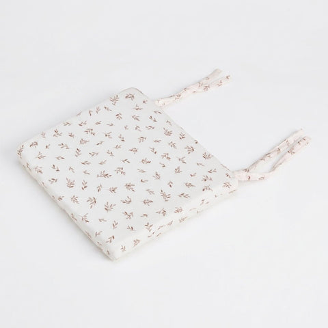 A KraftKids Sitzkissen für Stühle aus Musselin in hellem Creme mit feinem braunem Blattmuster und zwei Paar Stoffbändern auf einer Seite, rechteckig geformt, präsentiert auf weißem Hintergrund.