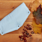 Eine blaue, handgenähte Stoffwindel mit Druckknöpfen ruht auf Holz, umgeben von Herbstblättern und Kastanien. Der weiche Fleece ist besonders kuschelig - ideal, um ihn an kühlen Tagen mit dem KraftKids Kinderwagenmuff kleine Blätter hellblau auf Weiß zu kombinieren.