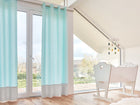 Ein helles, modernes Zimmer mit großen Fenstern, hellen Holzböden und KraftKids Gardinen "weiße Pfeile auf Mint Unigrau" aus 100% Baumwolle. Enthält einen kleinen weißen Schreibtisch und einen Stuhl sowie ein hängendes Wolkenmobile mit bunten Regentropfen.