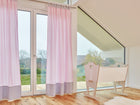 Ein helles Zimmer mit großen Fenstern, Holzboden und einer leichten Holzwiege am Fenster. KraftKids Gardinen Unigrau weiße Punkte auf Rosa verleihen dem Babyzimmer eine charmante Note - ideal für die Einrichtung mit Blick ins Grüne.