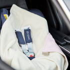 Eine KraftKids "Decke für Babyschale Winter kleine Blätter rosa auf Weiß" ist über einen auf dem Rücksitz eines Autos installierten Kindersitz drapiert. Der Gurt ist angelegt, und der Sitz scheint leer zu sein.