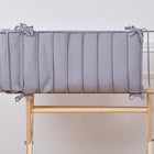 Die KraftKids Bettumrandung Nestchen Musselin grau Punkte ist eine handgefertigte graue Bettumrandung mit weißen Punkten, die aus 100% Baumwolle besteht und an einem Holzbett mit Metallrahmen befestigt ist, das vor einer weißen Wand mit Zierleisten steht.