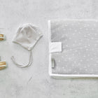 Ein Paar beigefarbene Babysandalen, eine grau-weiß gestreifte Babymütze mit Kinnriemen und eine gefaltete KraftKids Reisewickelunterlage Musselin grau Pusteblumen auf einer hellgrauen Betonfläche.