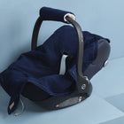 A KraftKids Babydecke für Babyschale Sommer Musselin in Dunkelblau liegt auf einer Babyschale mit gebogenem schwarzem Griff und blauem Bezug. Die Schale verfügt über ein Drei-Punkte-Gurt-System und steht auf einer hellblauen Fläche vor hellblauer Wand.