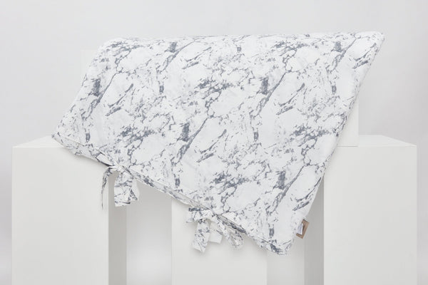 Der KraftKids Bezug für Wickeltischauflage weißer Marmor (75 x 70 cm) aus 100% Baumwolle zeigt drei Schleifen an einer Kante und wird auf einem schlichten, weißen geometrischen Ständer vor neutralem Hintergrund präsentiert.
