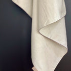 Eine hellgrün-weiße Leinen-Babydecke von KraftKids, mit einem kleinen Stoffanhänger, hängt in weichen Falten vor einem dunklen Hintergrund und erinnert an eine kuschelige Decke - perfekt, um jedem Raum Wärme zu verleihen.