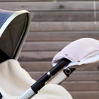 Eine Nahaufnahme eines Kinderwagens mit dem handgenähten KraftKids Kinderwagenmuff Doppelkrepp Rosa, der zur Erwärmung am Griff befestigt ist, vor dem Hintergrund eines Holzzauns.