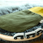 Ein KraftKids Strampelsack Frühling Sommer Doppelkrepp Grün Herbstgrün Babyschlafsack liegt auf einem weichen grauen Kunstfellteppich, umgeben von einer hölzernen Spielzeugeisenbahnstrecke mit einem kleinen weißen Zug.