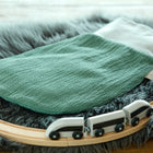 Ein KraftKids Strampelsack Herbst Winter Doppelkrepp Grün Jade Babyschlafsack ruht auf einem grauen Kunstfellteppich neben einer hölzernen Spielzeugeisenbahn mit einem weißen Zug.