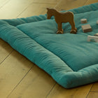 Eine KraftKids Krabbeldecke Doppelkrepp Grün Jade mit Polyestervlieseinlage liegt auf einem Holzboden. Holzspielzeug, darunter eine Pferdefigur und mehrere geometrische Blöcke, liegen auf der Matte.