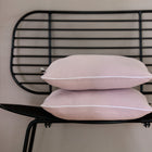 Zwei KraftKids Kissenbezug Doppelkrepp Rosa sind auf einem schwarzen Metallstuhl mit Gitterrückenlehne gestapelt, der vor einer beigen Wand steht.