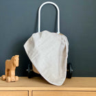 Ein Holzspielzeugpferd auf Rädern steht neben einem kleinen Weidenkorb mit weißen Griffen, der mit der KraftKids Babydecke Cord Breitcord in Beige Taupe drapiert ist, alles auf einer hellen Holzfläche vor einer dunklen Wand.