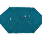 Die KraftKids Babydecke für Babyschale Sommer aus Musselin in Petrol mit goldenen Punkten ist sechseckig gefaltet, hat vier vertikale Schlitze für ein Drei-Punkte-Gurt-System und ein kleines beiges Markentag an einer Kante.