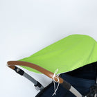 Ein KraftKids Sonnensegel weiße Punkte auf Grün mit weißen Schnüren bedeckt einen Kinderwagen mit dunklem Sitz und braunem Griff, der vor einem einfarbig weißen Hintergrund abgebildet ist.