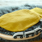 Der KraftKids Strampelsack Frühling Sommer Doppelkrepp Gelb Senf ruht auf einem grauen Kunstfellteppich inmitten einer hölzernen Spielzeugeisenbahn mit einem kleinen weißen und schwarzen Spielzeugeisenbahnzug auf den Schienen.