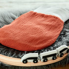 Ein KraftKids Strampelsack Frühling Sommer Doppelkrepp Rot Herbstrot Babyschlafsack liegt auf einem grauen Kunstfellteppich, umgeben von einer hölzernen Spielzeugeisenbahnstrecke mit einem weißen Spielzeugeisenbahnzug.