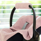 Eine KraftKids Babydecke für Babyschale Sommer Doppelkrepp Rosa ist über einen Babyautositz drapiert, der vor einem hellen Fenster mit horizontalen Jalousien steht.