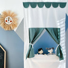 Ein Kinderzimmer mit einer blauen und grauen geometrischen Wand, einer Dekoration mit einem lächelnden Löwengesicht, einer Kreidetafel mit Zeichnungen und dem KraftKids Puppentheater Kasperletheater Doppelkrepp Grün Jade inkl. Teleskopstange. Teleskopstange mit zwei Stoffpuppen.