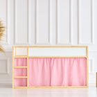 Ein modernes Kinderbett mit hellem Holzrahmen und KraftKids Hochbettvorhänge Set 2+1 Musselin rosa für Kura Bett steht vor einer weiß getäfelten Wand. In der Nähe bereichern eine geflochtene Vase mit Pampasgras und zwei hölzerne Würfelhocker die Raumgestaltung.